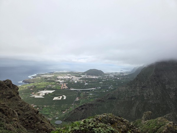Panoramablick über Buenavista del Norte mit grünen Feldern, Häusern, Steilküsten und tief hängenden Wolken.