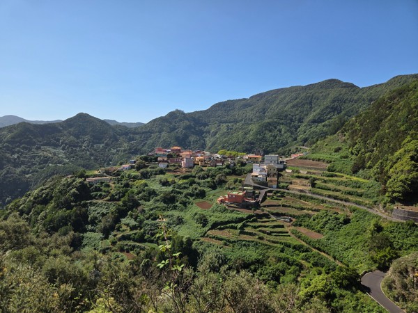 Blick auf Carboneras mit terrassierten Feldern, bunten Häusern und grünen Berghängen unter klarem blauem Himmel.