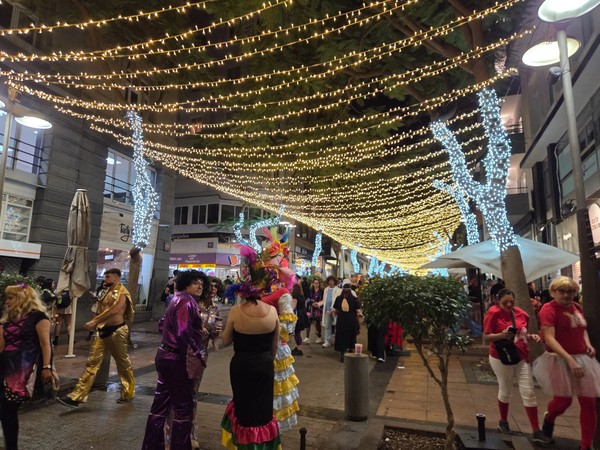 Eine festlich beleuchtete Straße in Santa Cruz de Tenerife mit Karnevalsbesuchern und bunten Kostümen bei Nacht.