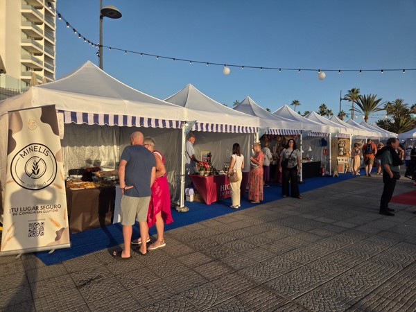 Reihe weißer Marktstände auf einer Promenade in Costa Adeje bei warmem Abendlicht mit Besuchern und Palmen im Hintergrund.