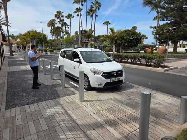 Weißes Taxi an einer Straße in Costa Adeje, umgeben von Palmen, Gehwegpfosten und gepflegten Grünanlagen.