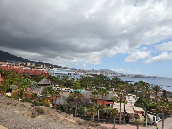 Panoramablick über Costa Adeje mit Hotels, Palmen, Küste und bewölktem Himmel über dem Atlantik.