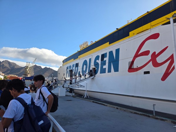 Passagiere gehen über die Gangway auf eine große Fred-Olsen-Fähre im Hafen, vor Bergen und blauem Himmel.