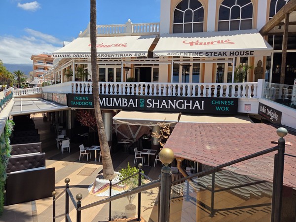 Außenansicht eines Restaurantbereichs mit den Lokalen Taurus und Mumbai to Shanghai an einer sonnigen Promenade auf Teneriffa.