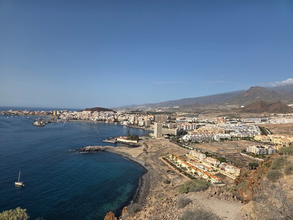 Weitblick über Los Cristianos mit Hafen, Küste, Wohnanlagen und trockenem Gelände im Sonnenlicht.