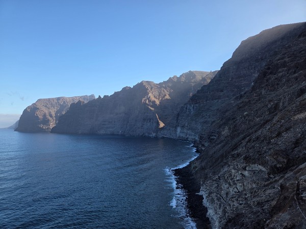 Die steilen Felswände von Los Gigantes ragen dunkel über dem ruhigen Meer an der Westküste Teneriffas auf.