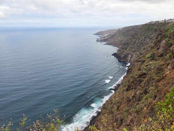 Steile Küste bei La Garañona mit dunklem Strand, ruhigem Meer und hohen Klippen unter bewölktem Himmel.