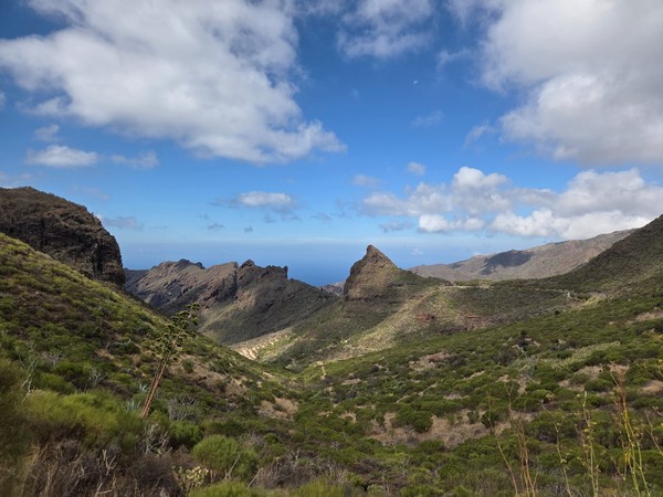 Weite Aussicht über grüne Berge und Täler bis zum Atlantik unter blauem Himmel mit großen Wolken.
