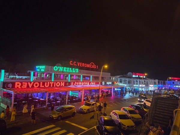 Bunte Neonlichter und belebte Bars in einer Ausgehstraße bei Nacht auf Teneriffa.