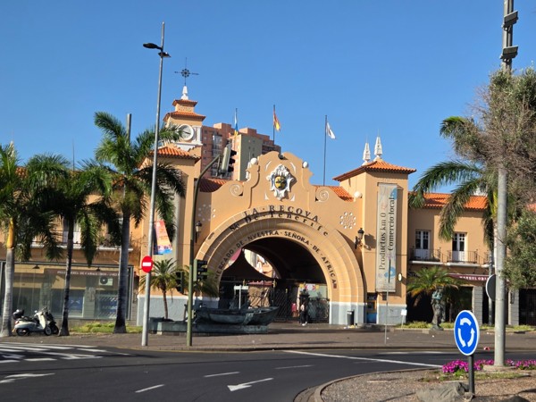 Der Eingang des Marktes Nuestra Señora de África in Santa Cruz de Tenerife steht unter blauem Himmel zwischen Palmen und Straßenverkehr.