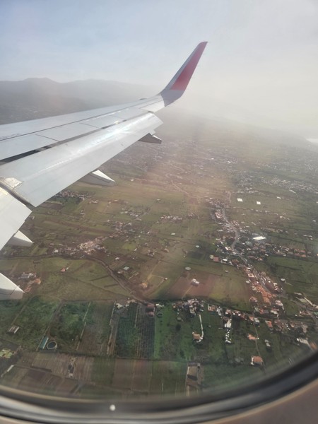 Blick aus dem Flugzeugfenster auf Tragfläche, ländliche Landschaft und diesige Wetterstimmung beim Landeanflug auf den Flughafen Teneriffa Nord.