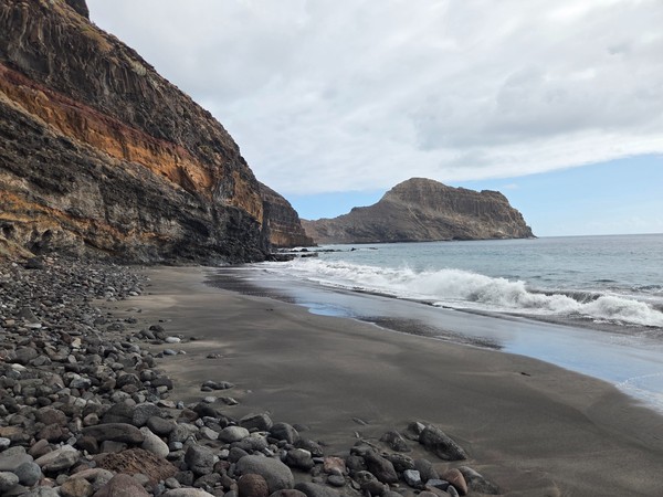 Schwarzer Sandstrand Playa de Aitamar mit Felsen, Brandung und einer markanten Felsinsel im Hintergrund.