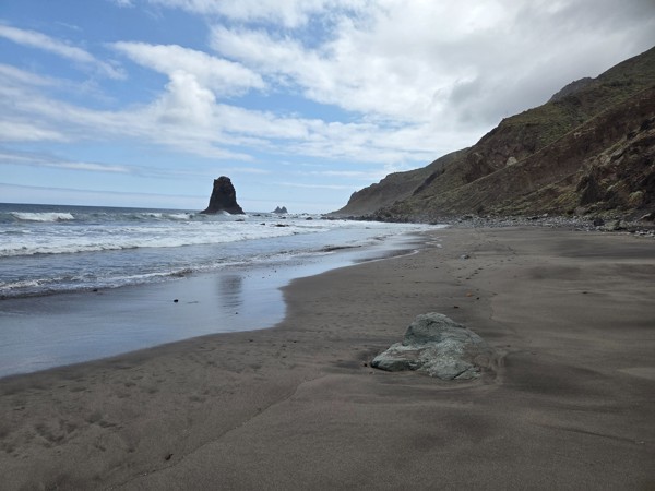 Schwarzer Sandstrand von Benijo mit Brandung, Felsen im Wasser und rauer Küstenlandschaft.