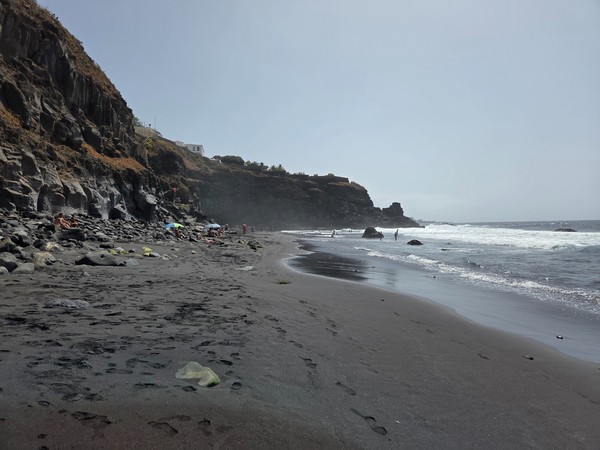 Schwarzer Sandstrand Playa de Ancón mit Felsen, Wellen und einigen Badegästen an der Küste von Teneriffa.