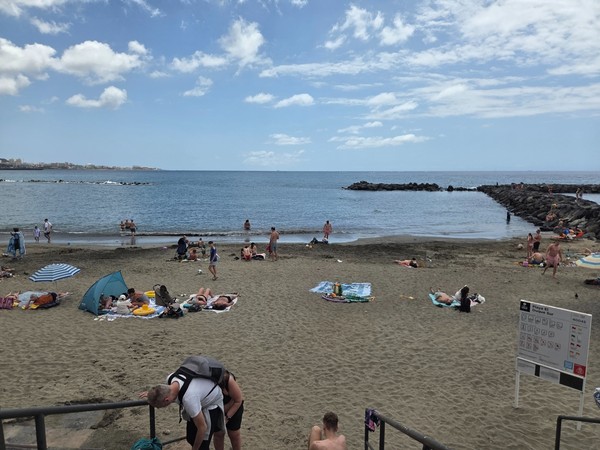 Badegäste an der Playa El Duque mit ruhigem Meer, Wellenbrechern und Strandbereich an der Costa Adeje.