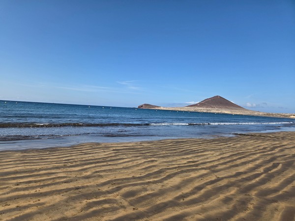 Sandstrand bei El Médano mit Blick auf die Montaña Roja, ruhigem Meer und klarer, sonniger Atmosphäre.