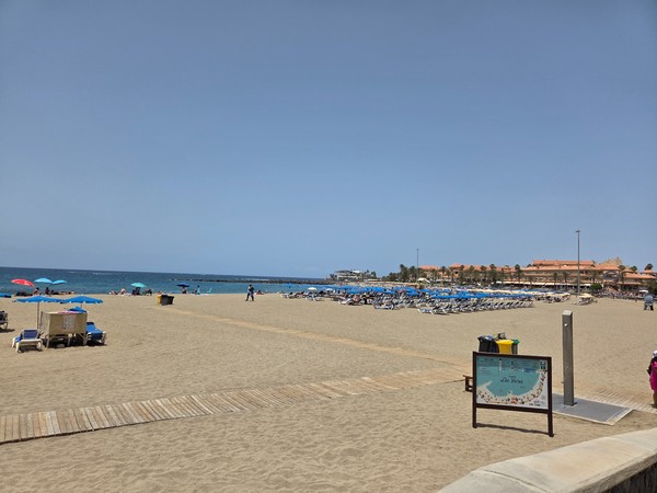 Der breite Sandstrand Playa Las Vistas mit Liegen, Sonnenschirmen und ruhigem Meer an einem klaren Tag.