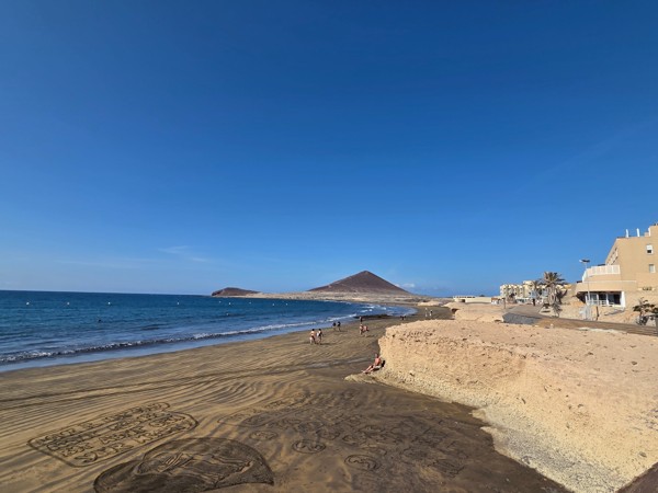 Der weite Sandstrand von El Médano mit Blick auf den markanten Montaña Roja unter klarem blauem Himmel.