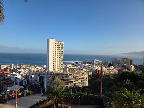 Blick über Puerto de la Cruz mit Hochhäusern, Atlantik und Küstenlinie in warmem Morgen- oder Abendlicht.