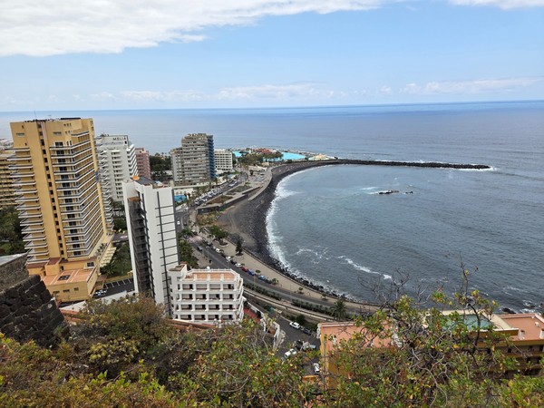 Blick von oben auf die Küste von Puerto de la Cruz mit Hotels, Uferstraße und einer geschwungenen Mole am Atlantik.