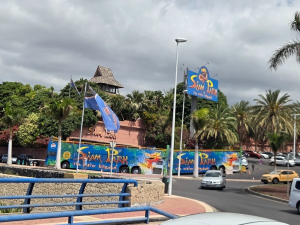 Außenansicht des Siam Park mit großem Schild, Palmen, parkenden Autos und dunklen Wolken über dem Gelände.