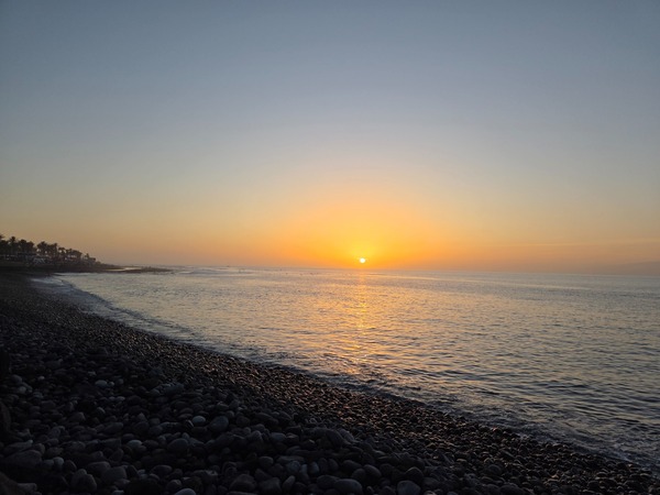 Sonnenuntergang an der Küste von Costa Adeje mit dunklem Kiesstrand, ruhigem Meer und warmem Abendlicht.
