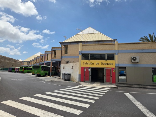 Busbahnhof in Costa Adeje mit der Aufschrift Estación de Guaguas, mehreren grünen Bussen und Zebrastreifen im Vordergrund.